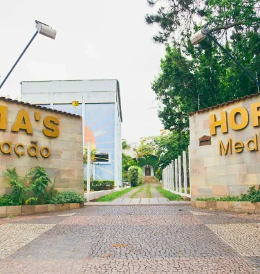 Entrada da Fundação Cima’s em São Lourenço, Minas Gerais, marcada por paredes de pedra com inscrições douradas que dizem: " Cima's Fundação" e " Horto Medicinal. Um caminho de paralelepípedos e vegetação exuberante, refletindo a rica história e legado do Professor Cima antes de seu falecimento em 2015.