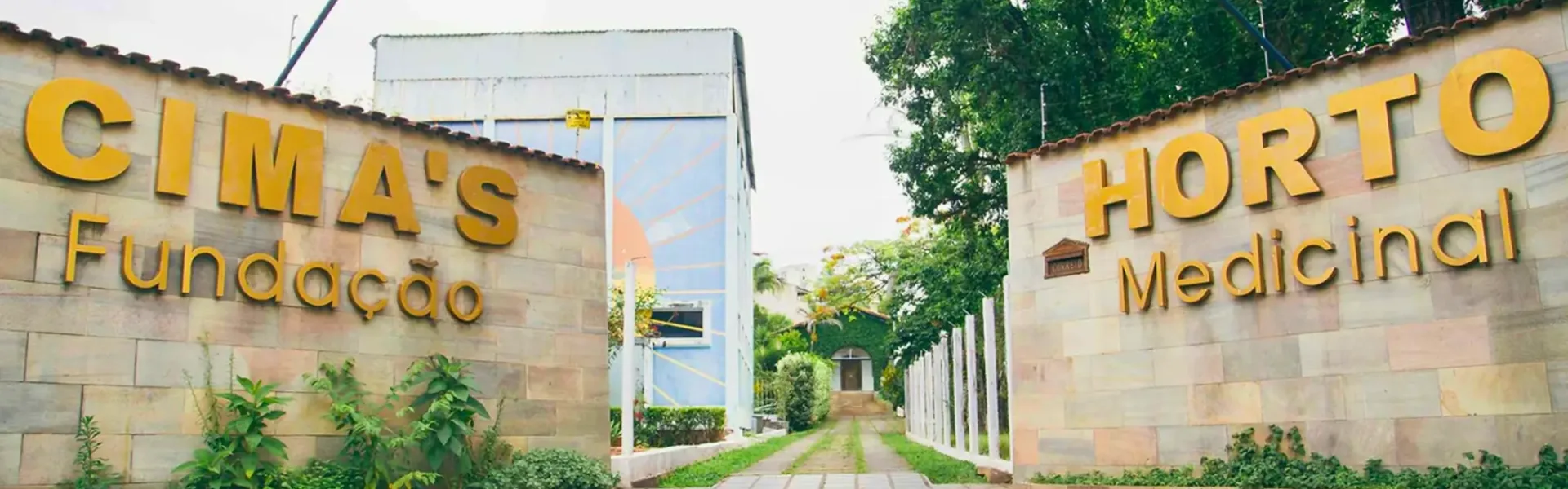 Entrada da Fundação Cima’s em São Lourenço, Minas Gerais, marcada por paredes de pedra com inscrições douradas que dizem: " Cima's Fundação" e " Horto Medicinal. Um caminho de paralelepípedos e vegetação exuberante, refletindo a rica história e legado do Professor Cima antes de seu falecimento em 2015.